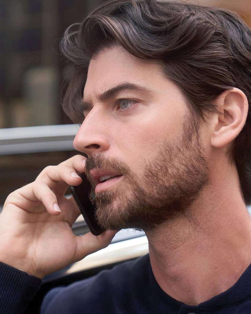 Чоловік тримає телефон біля вуха, стоячи перед автомобілем Peugeot